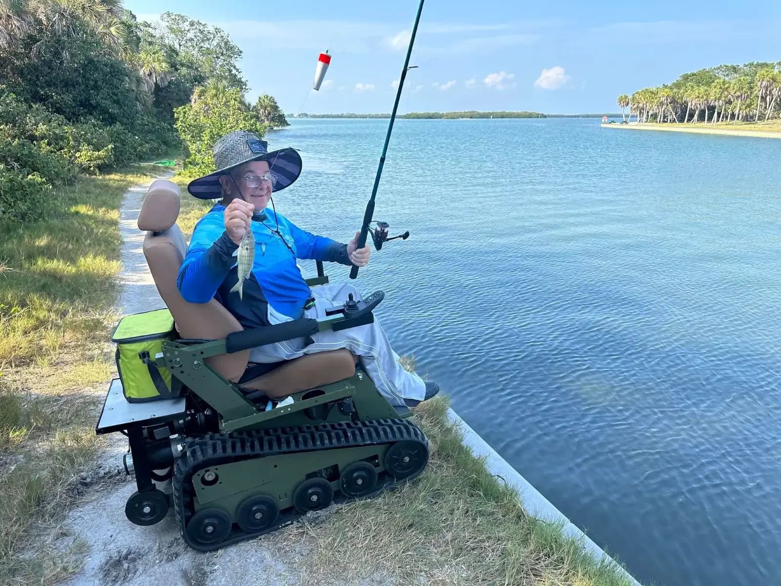 A rider holding up a fish they just caught while seated in an EcoRover beside a Florida waterway.