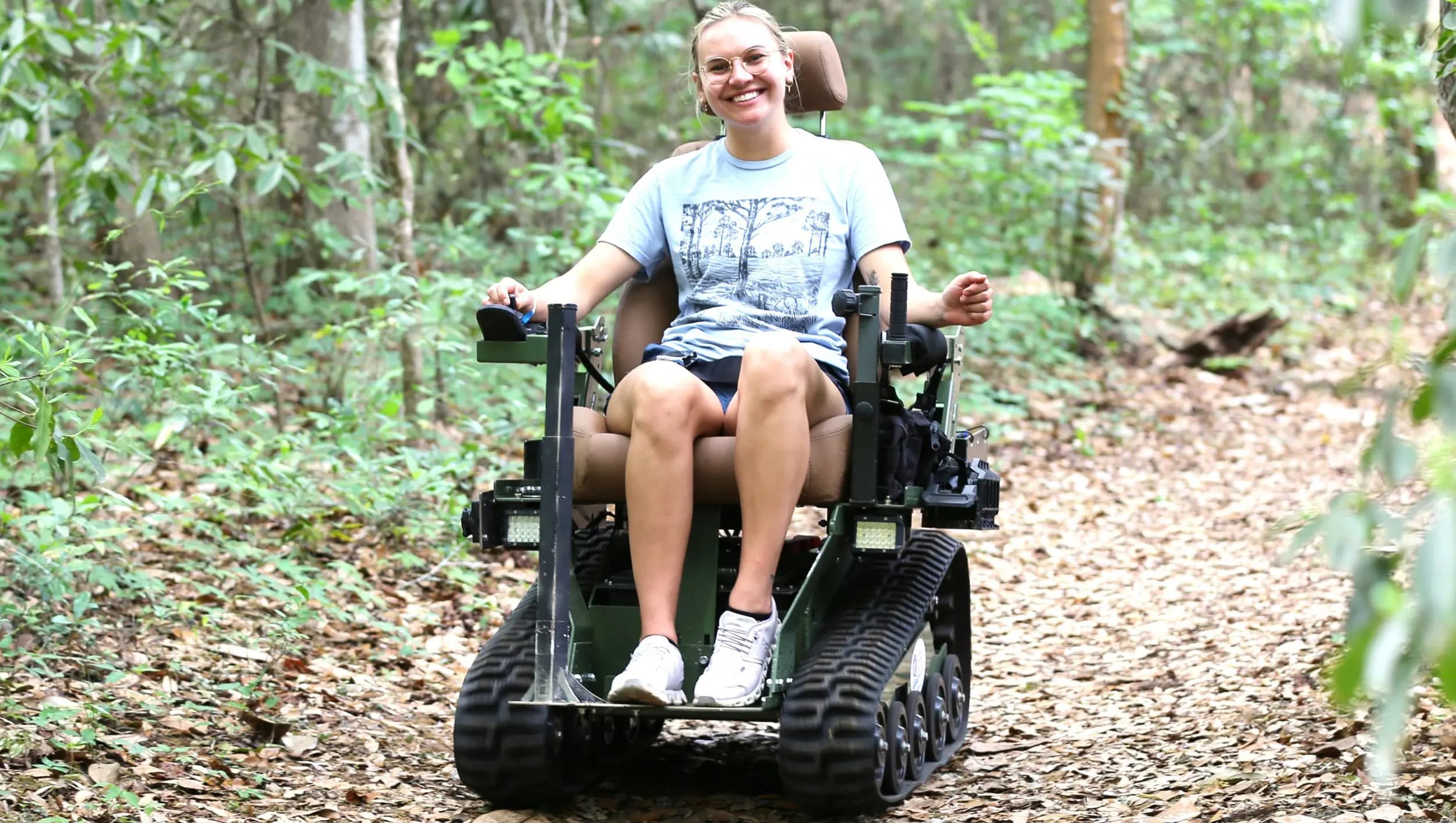 A woman smiling broadly while riding an EcoRover down a sunlit forest trail.