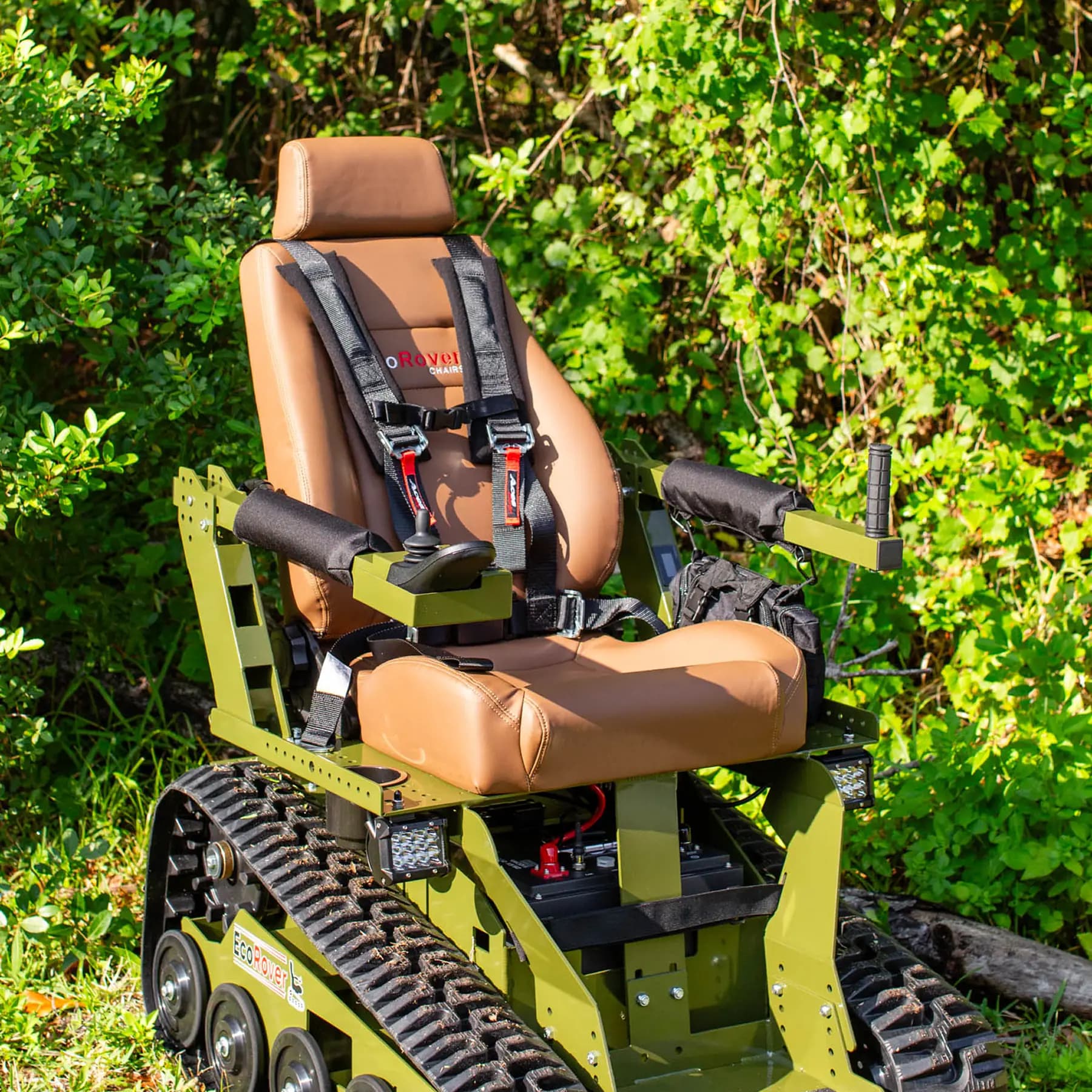 An EcoRover with tan leather upholstery and harness, parked in front of lush green foliage.