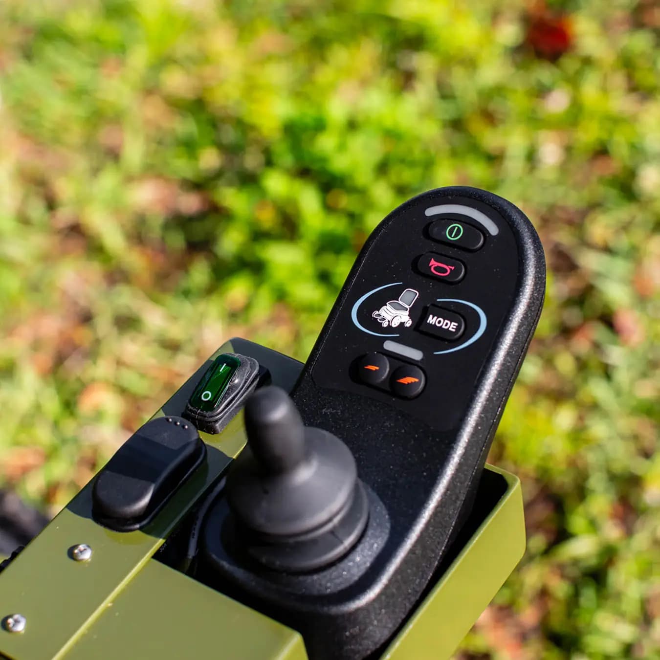 Close-up of an EcoRover joystick control panel with mode buttons against a green outdoor background.