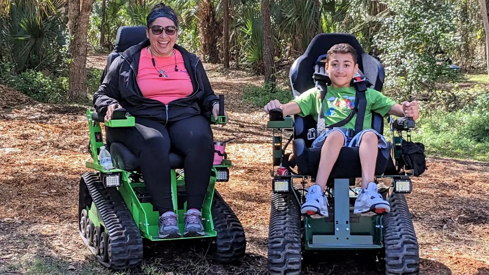 A woman and a young boy riding side by side in EcoRovers on a shaded Florida trail, both smiling.